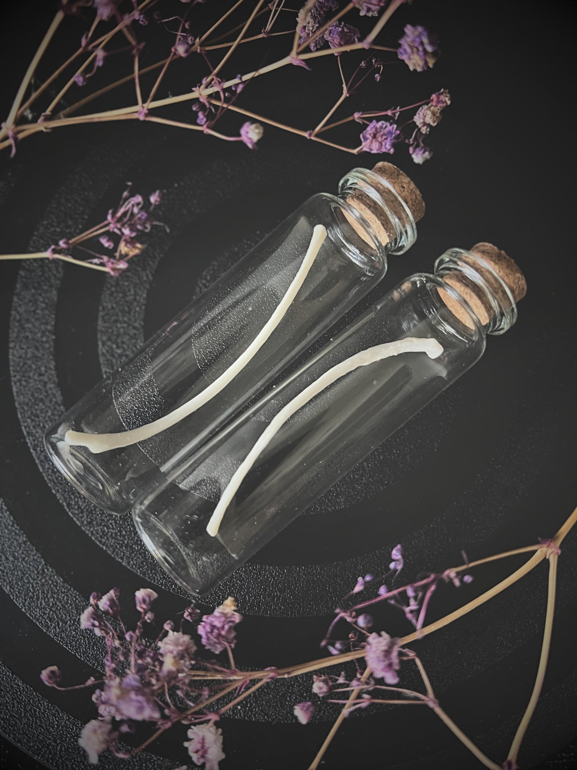 Two glass bottles with cork lids containing fox rib bones on a dark background with dried flowers.